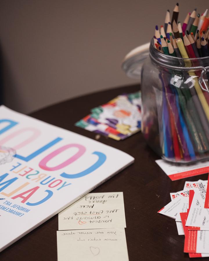 Materials sit on a table in the Counseling Center's waiting room, including a variety of colored pencils, a workbook that reads "Color Yourself Calm," business cards for Legal Aid of Nebraska and sticky notes from other students that read "I'm happy you're here," "the first step is always the hardest [heart emoji]," "you are never alone" and "nunca estás solo."